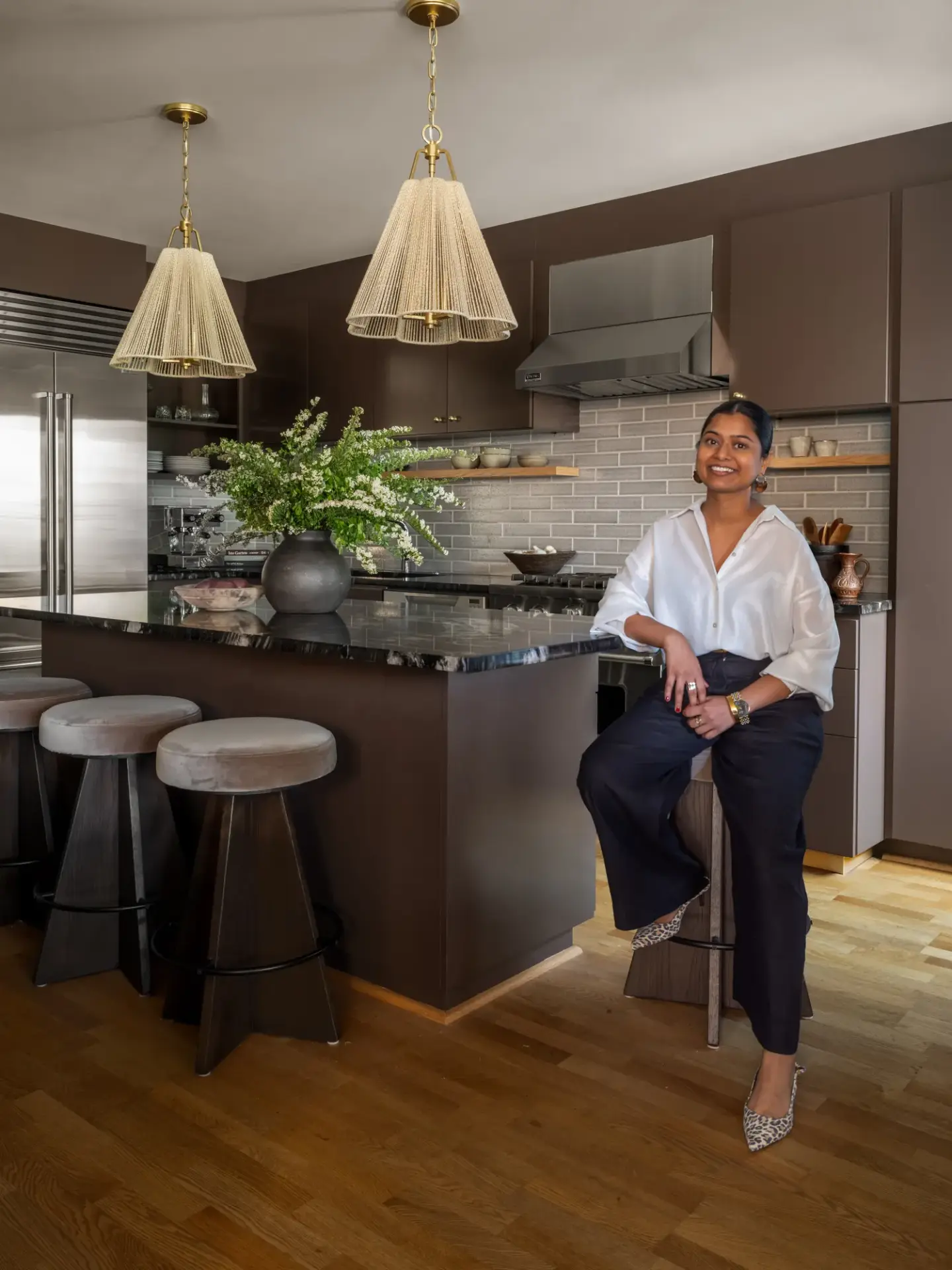 Neha Gupta of NU Curations seated at the marble island of a Queen Anne kitchen she designed